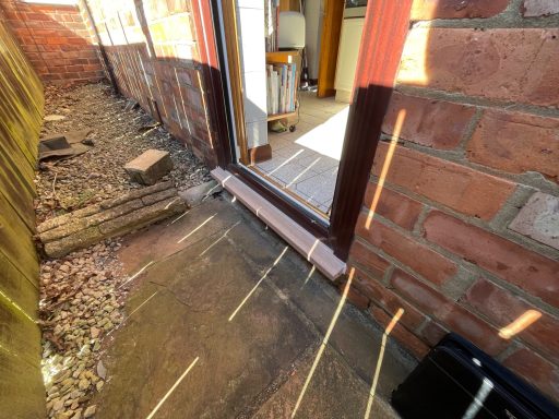 View of a narrow pathway with gravel and wooden logs leading to an open door.