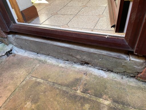 A close-up of a weathered door threshold and adjacent stone floor.