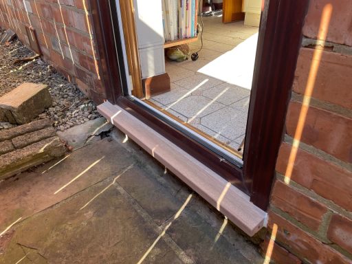 A brown door threshold against a brick wall with light streaming in from a doorway.
